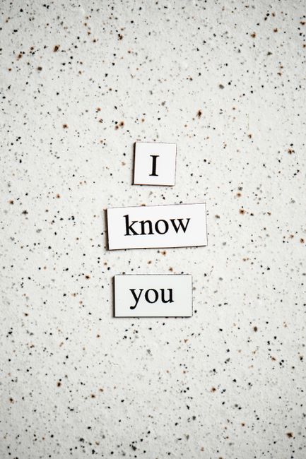 A close-up image of a speckled white tabletop surface with small brown and black flecks, where three white rectangular tiles are arranged vertically. The tiles display black printed text spelling out